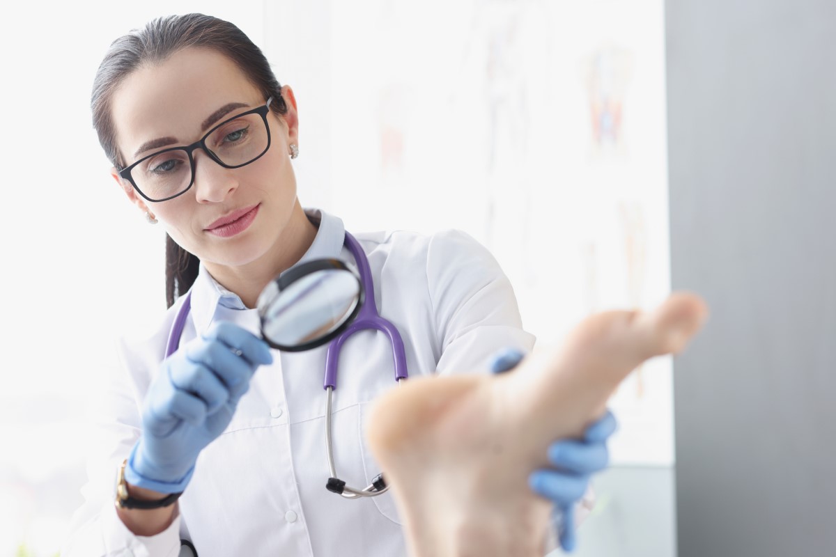 Examen de la piel del pie por un médico utilizando una lupa.