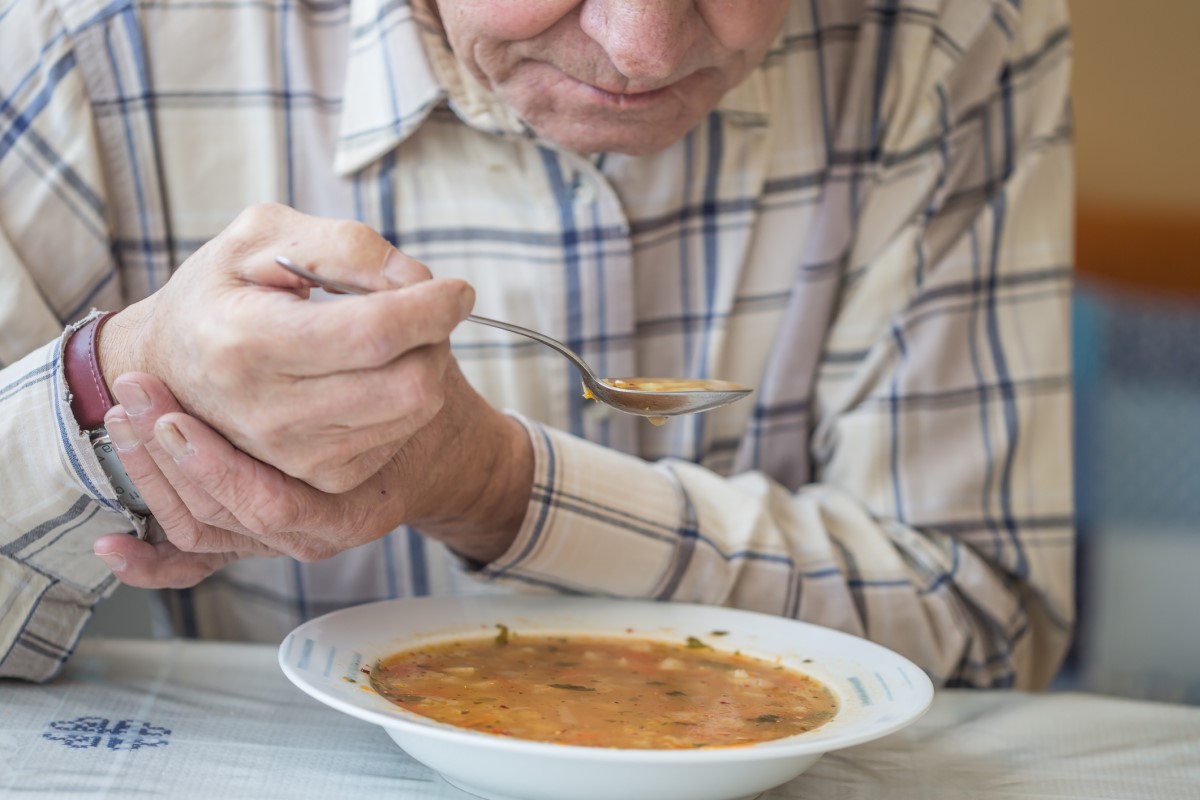 Un hombre toma sopa y sujeta su mano contra los temblores de la enfermedad de Parkinson