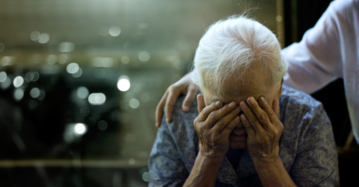 Una anciana tiene un problema de salud, tiene la cabeza apoyada en los brazos y una persona le sujeta los hombros