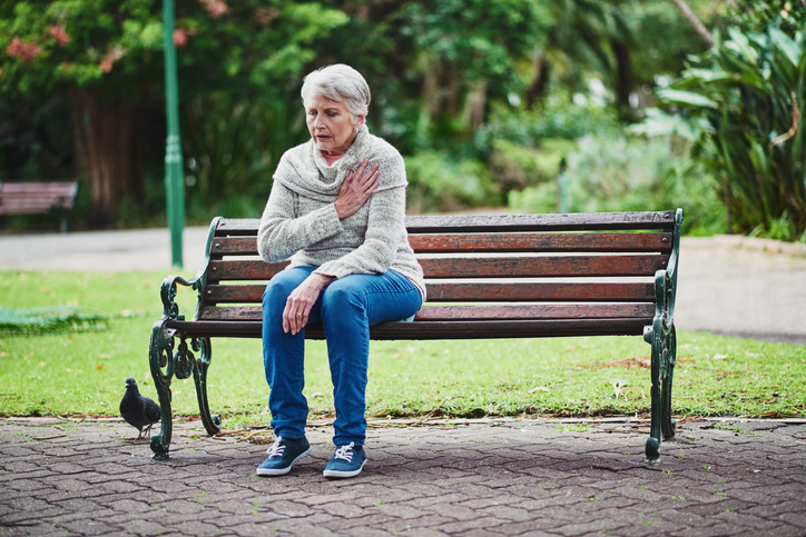 Una anciana está sentada en un banco y tiene problemas de corazón.