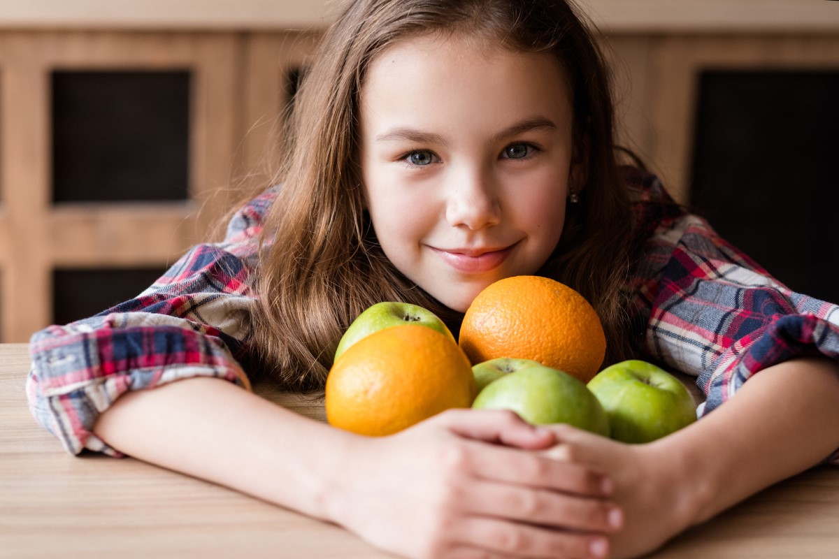 Vitamina C, en las frutas, un niño con naranjas y manzanas en los brazos