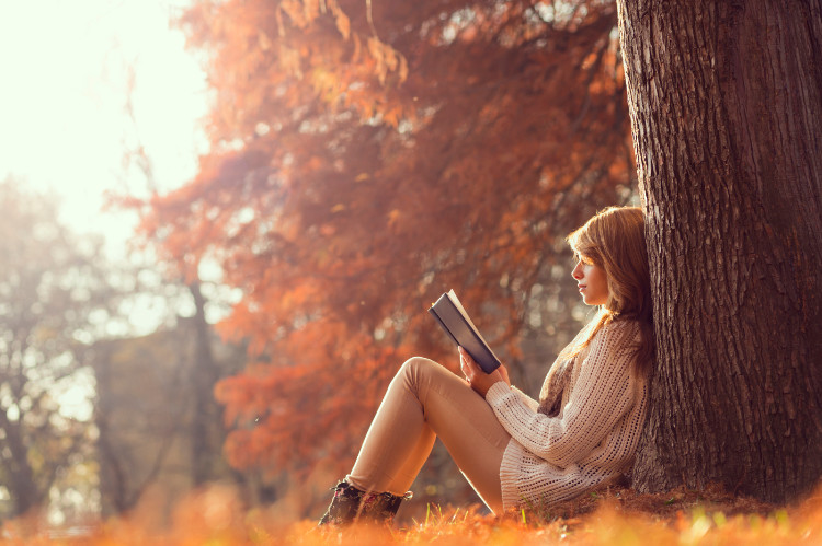 mujer sentada en el bosque, apoyada en un árbol leyendo un libro en otoño