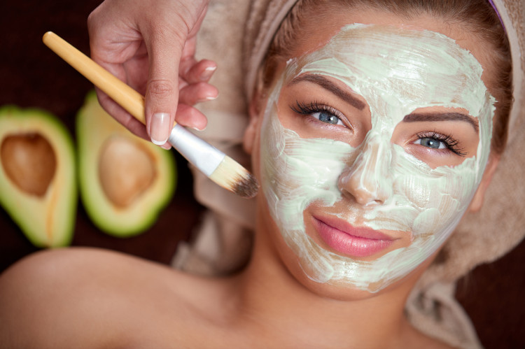 mujer con turbante en la cabeza y máscara verde natural en la cara, al fondo hay un aguacate cortado