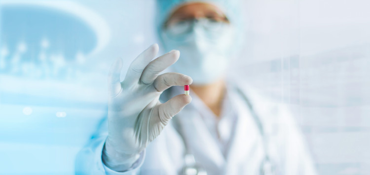 una doctora con uniforme blanco y velo en la cara que sostiene una pastilla en la mano