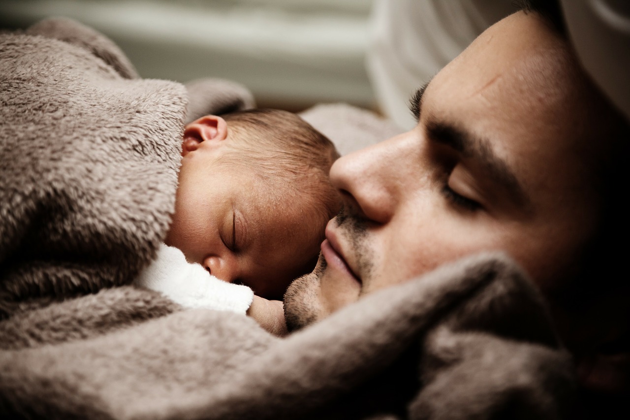 el bebé duerme junto a su padre bajo una manta marrón