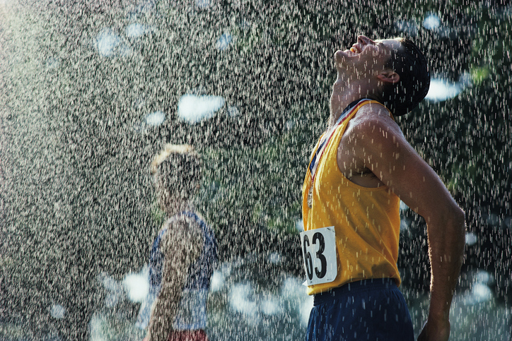 Un atleta masculino tras cruzar la línea de meta. Está lloviendo. Su cabeza está girada hacia arriba contra las gotas que caen. Tiene los ojos cerrados y lleva una medalla colgada del cuello. Lleva una camiseta de tirantes amarilla con el número 63 y pantalones cortos azules.