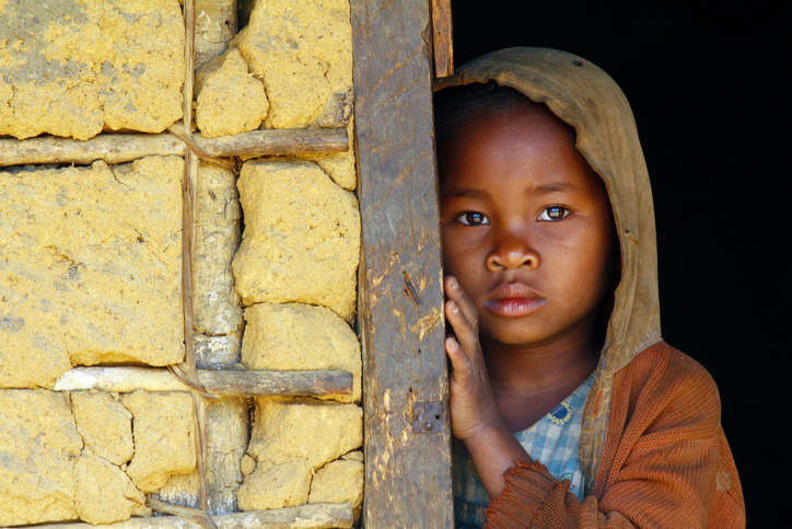 Un pobre niño negro con una mirada triste en su sudadera con capucha apoyado contra la pared.