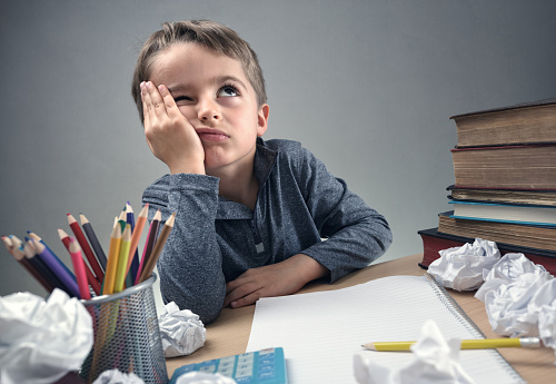 un escolar sentado en su pupitre, pensando en algo, con un cuaderno, papel y lápices en su pupitre