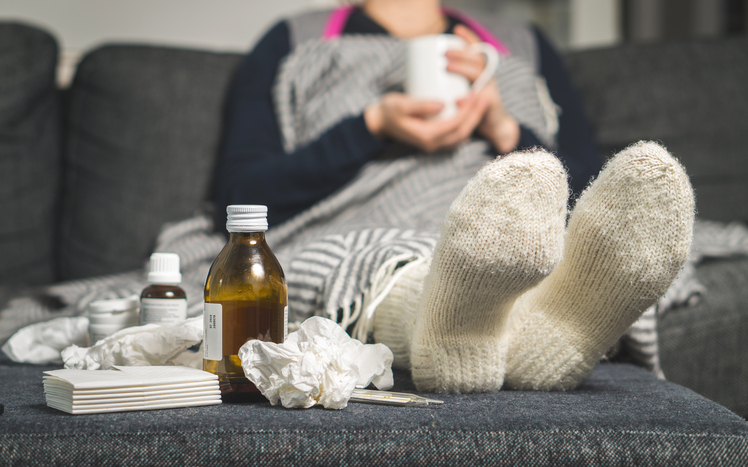 una mujer enferma está tumbada en la cama con calcetines calientes y pastillas y jarabes a su lado