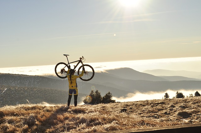 Una ciclista levanta su bicicleta por encima de la cabeza. Al fondo se ven montañas entre la niebla.