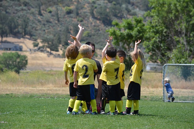 Niños con camisetas amarillas en el campo de fútbol. Disfrutando en grupo con su entrenador.