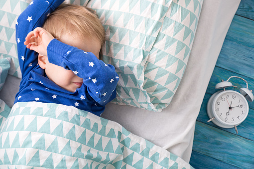 Niño despierto en pijama azul, junto al despertador