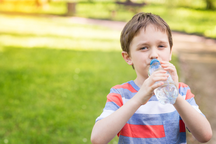 Niño bebiendo agua de una botella, hierba verde al fondo