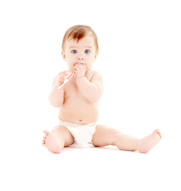 Un niño pequeño en pañal está sentado, con un cepillo de dientes en las manos, que tiene en la boca