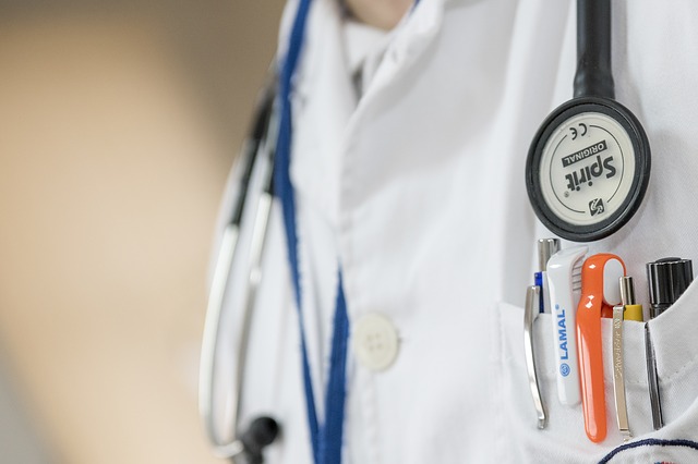 Recorte del torso de un médico, bata blanca, fonendoscopio, bolígrafos