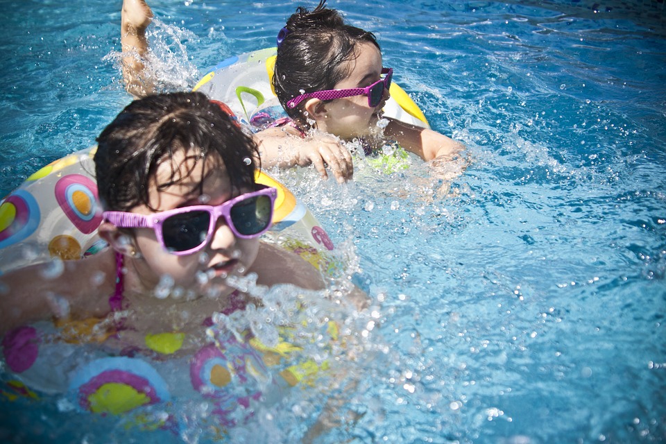 Dos niños nadan en el agua. Llevan gafas de sol con montura rosa. Van en bicicletas flotantes.