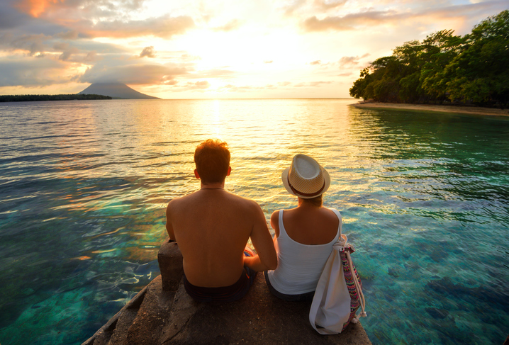 pareja sentada en una roca junto al mar al amanecer