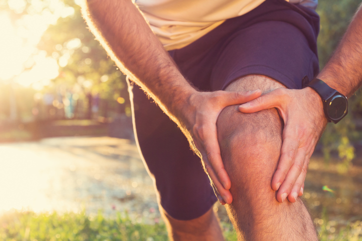 atleta masculino sujetándose la rodilla dolorida