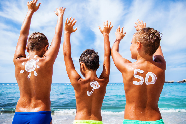 Protector solar para niños con OF 50, los niños están en la playa junto al mar y disfrutando, tienen las manos levantadas