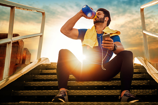 Un atleta sentado en las escaleras. Atardecer. Bebiendo un suplemento nutricional de un tarro.