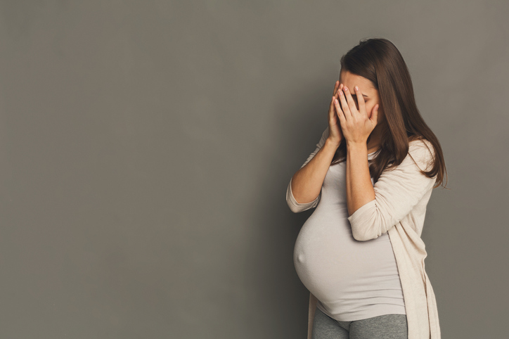 Una mujer embarazada cansada, cubriéndose la cara con las manos.