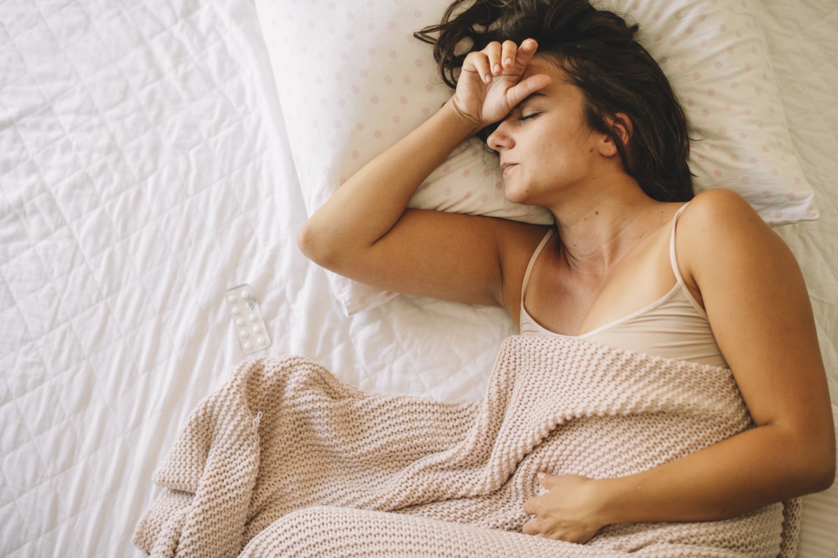 Una mujer cansada tumbada en la cama, le duele el estómago