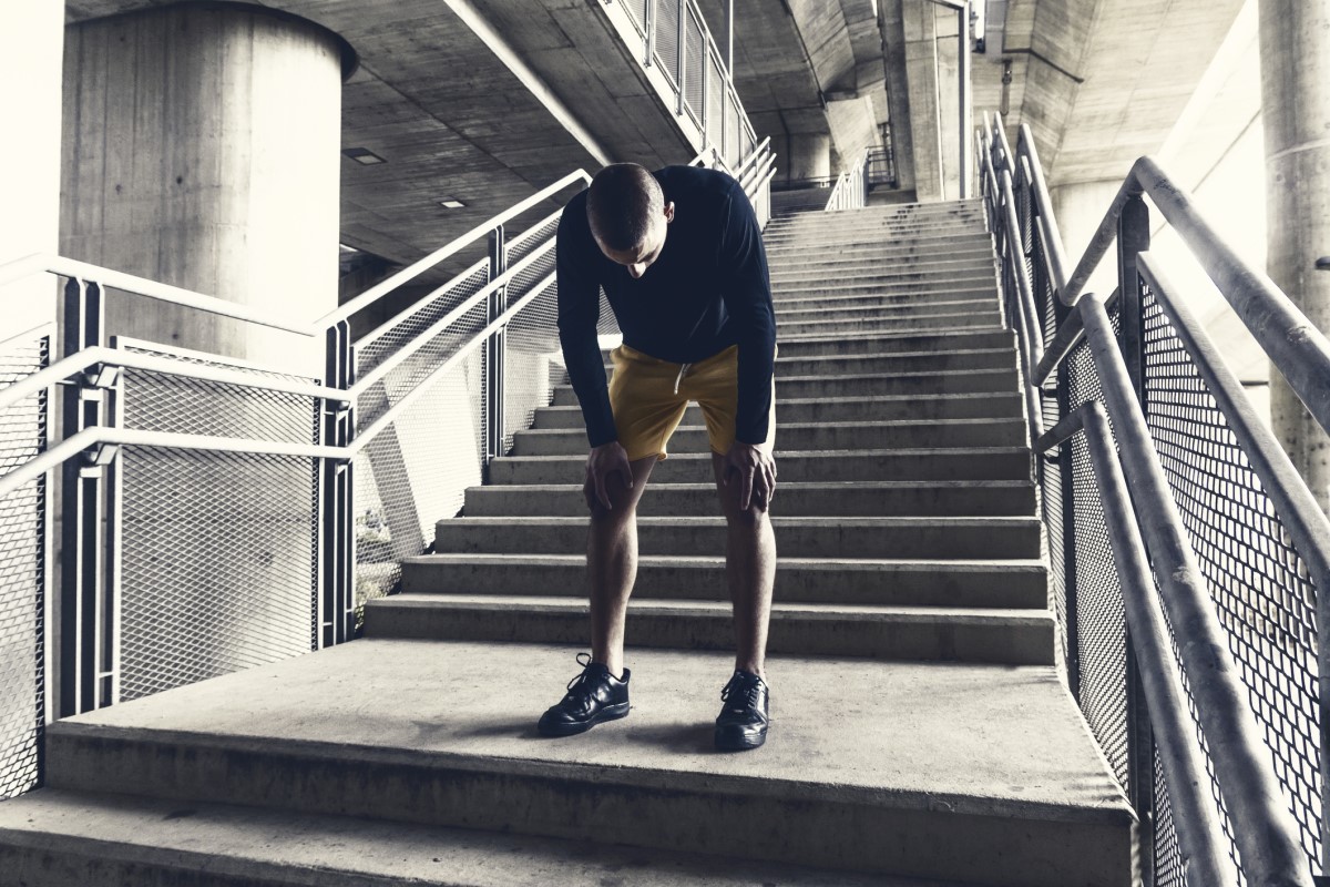 Un corredor cansado, un hombre, descansa bajo las escaleras después de un entrenamiento.