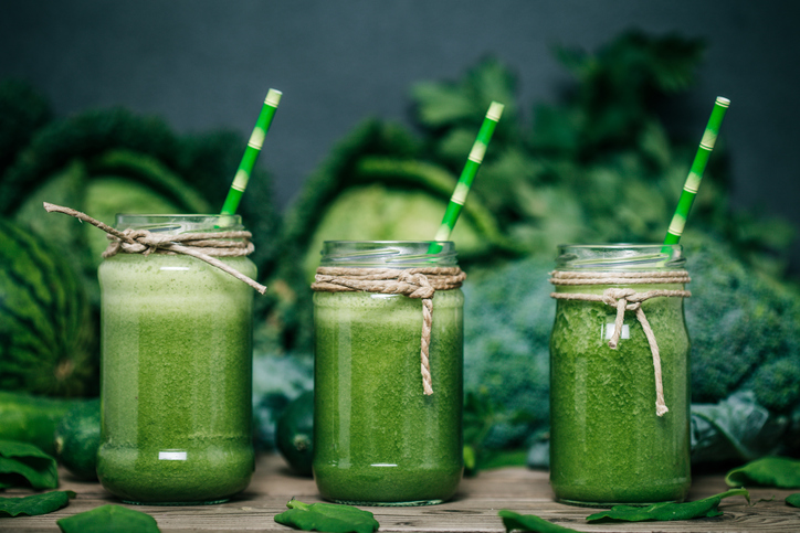 Batido de verduras verdes, tres vasos, col, brócoli y guisantes al fondo