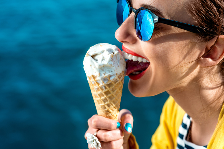 mujer con gafas de sol lamiendo helado junto al agua