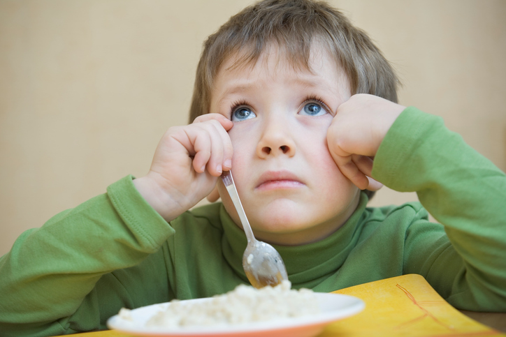 El niño se sienta encima del plato, no quiere comer, tiene un trastorno de la deglución debido a una inflamación en la cavidad oral