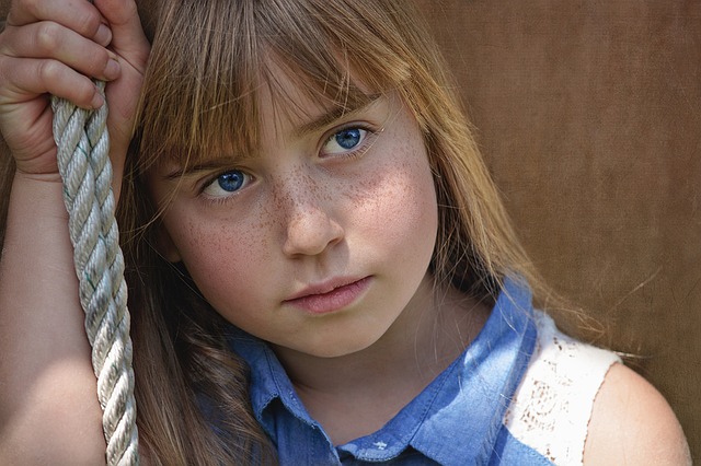 una joven sentada en un columpio, con mirada neutra, ojos azules