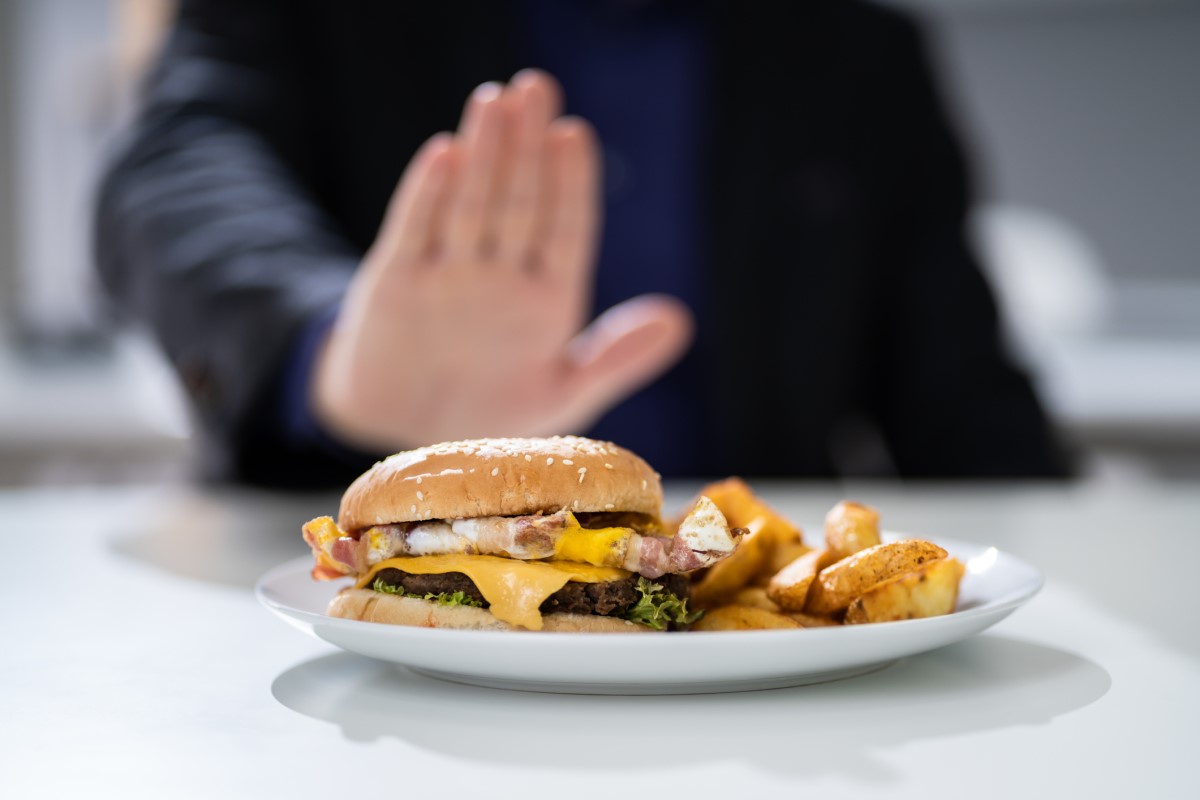 Alimentos inadecuados como causa de acidez estomacal: una hamburguesa en un plato que un hombre rechaza