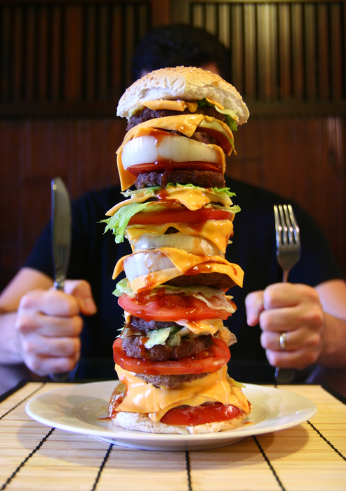 Un hombre se sienta a la mesa con una hamburguesa alta en el plato, una megafuerte