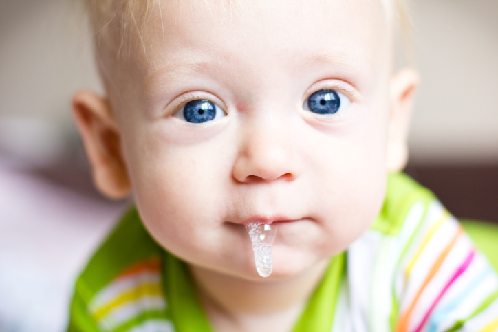 Un niño pequeño, un bebé, babea, le sale su primer diente