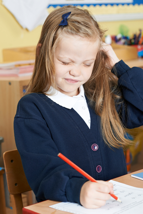 Una niña sentada en el colegio con picores en la cabeza, probablemente piojos en el pelo, rubia, sentada y escribiendo