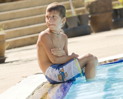 El chico está sentado junto a la piscina, con los pies en el agua. Tiene frío.