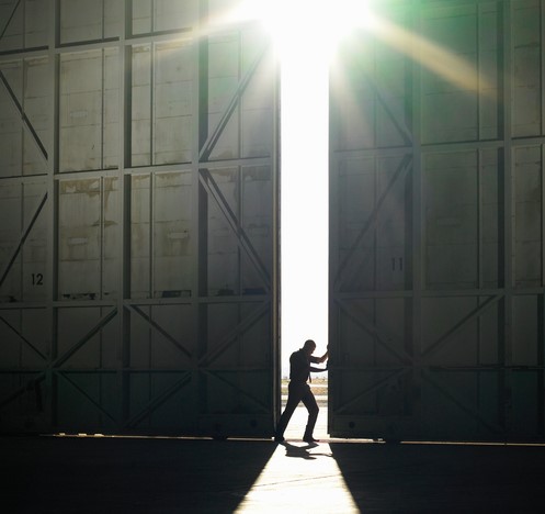 Un hombre sale de un pasillo oscuro a la luz del día, el sol brilla, abre una puerta en el pasillo