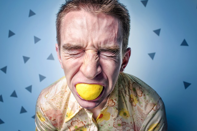 el hombre con el limón en la boca tiene una expresión facial agria, posiblemente una reacción alérgica a los cítricos