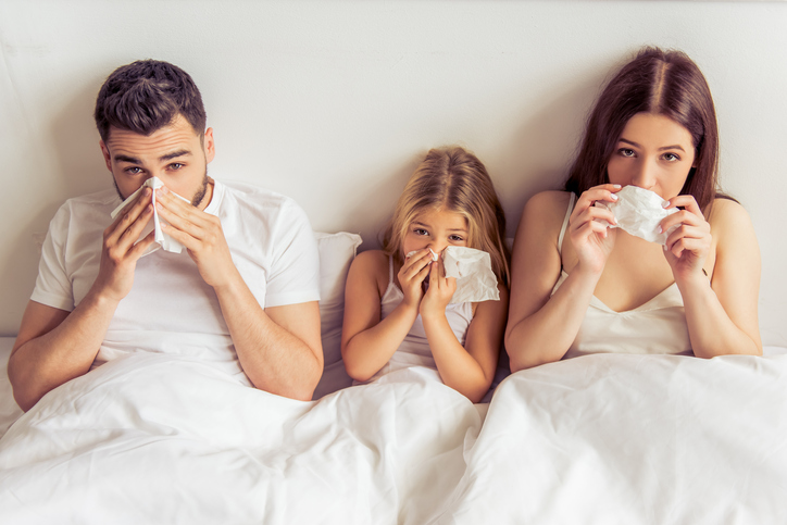 La familia, es decir, el padre, la madre y la hija están tumbados en la cama, tienen la nariz tapada, están resfriados, a causa de una enfermedad, por ejemplo, la gripe