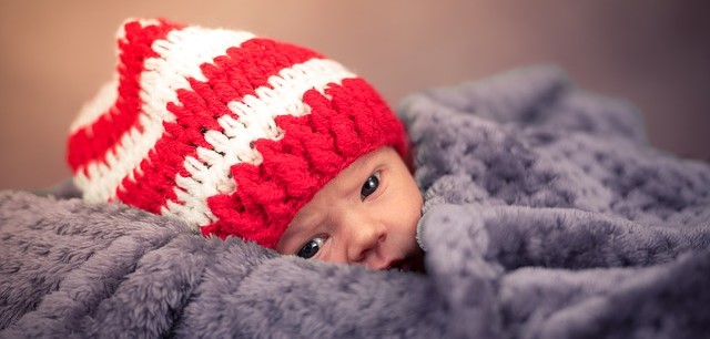 Un niño, tumbado y cubierto, con una gorra a rayas rojas y blancas