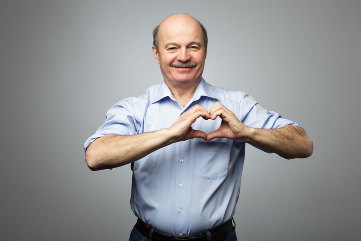 El hombre mayor tiene las manos sobre el pecho en forma de corazón, tiene una expresión de felicidad en la cara