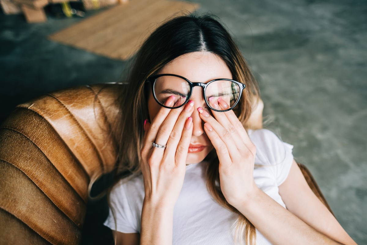 Una mujer cansada yace en el sofá, sosteniéndose los ojos.