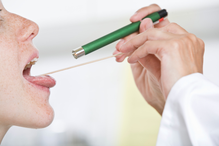 el médico examina la garganta de la mujer con un mazo bucal y sus ojos, iluminando la garganta con una linterna