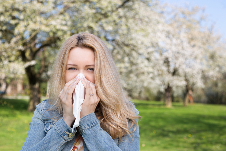 mujer tiene fiebre del heno, estornuda, está al aire libre, hierba y flores de árboles