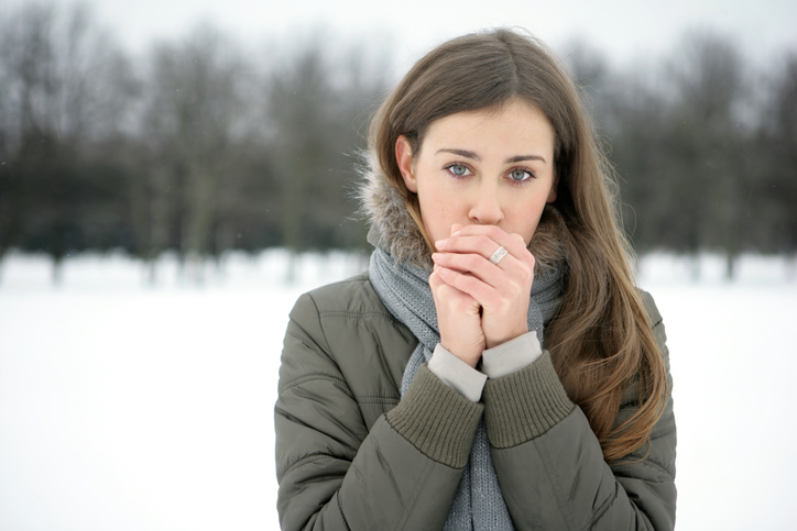 Una mujer calienta sus fríos miembros con su aliento, está nevando fuera, frío, frío